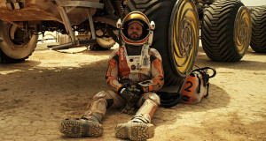 Mark Watney sits despondently in front of his rover vehicle in a scene from The Martian.